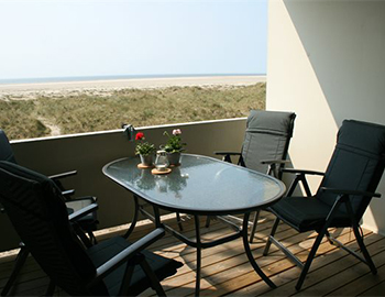 Altan med bord og fire stole. Fra altanen er der udsigt over klitterne, stranden og havet